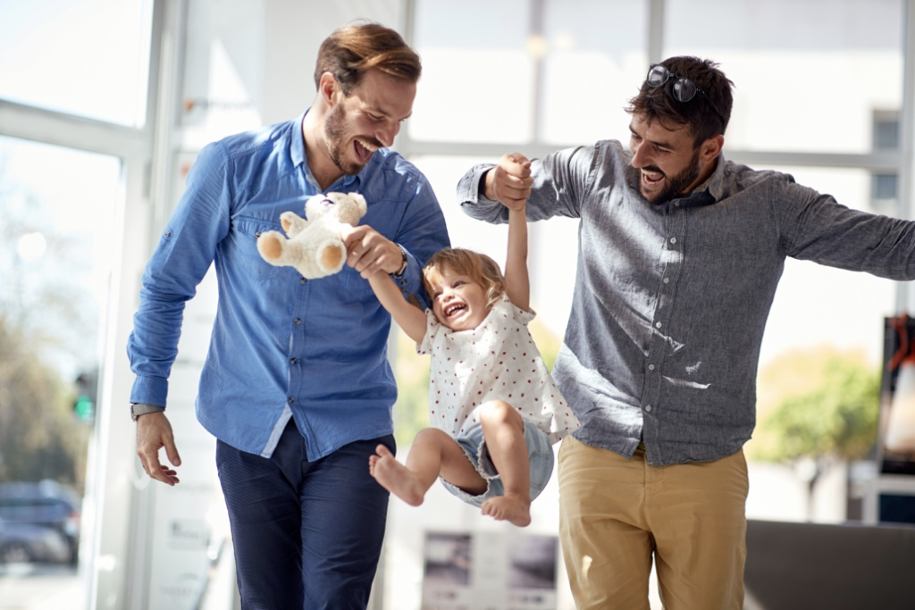 Two men holding hands with a child, lifting her playfully into the air.